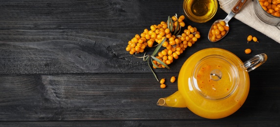 Image of Delicious sea buckthorn tea and fresh berries on black wooden table, flat lay. Banner design with space for text