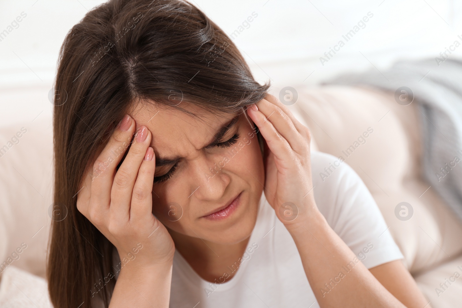 Photo of Young woman suffering from migraine on sofa at home