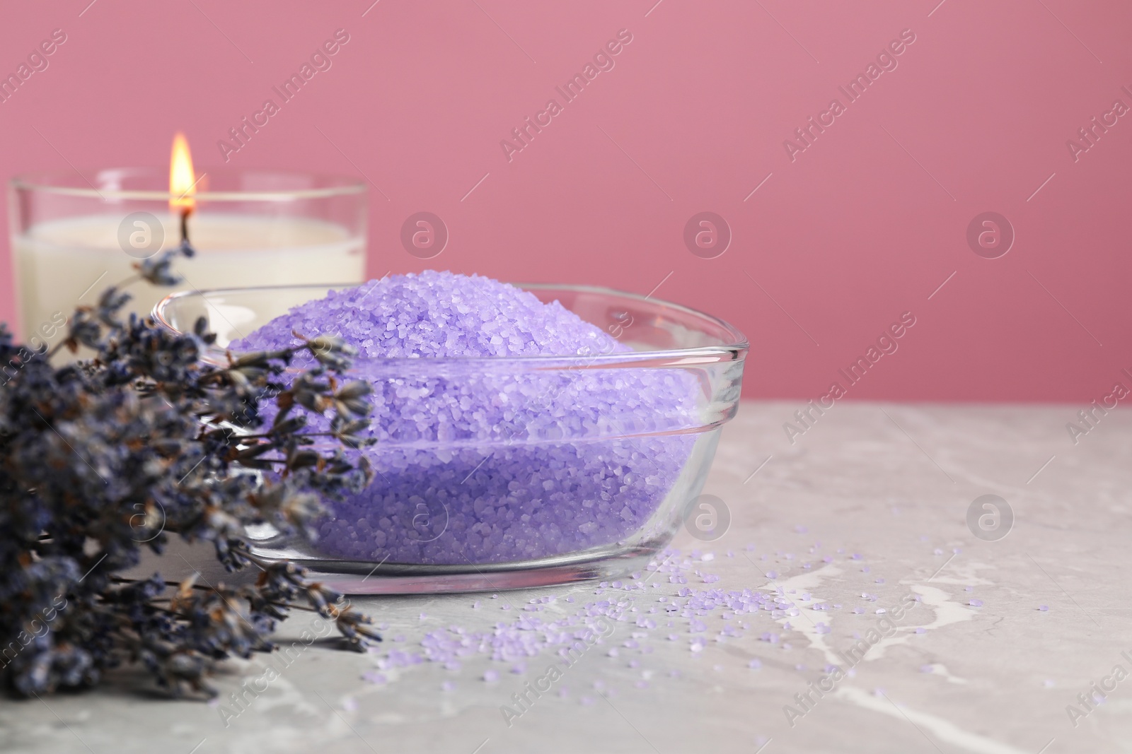 Photo of Violet sea salt in bowl, lavender flowers and burning candle on grey marble table. Space for text