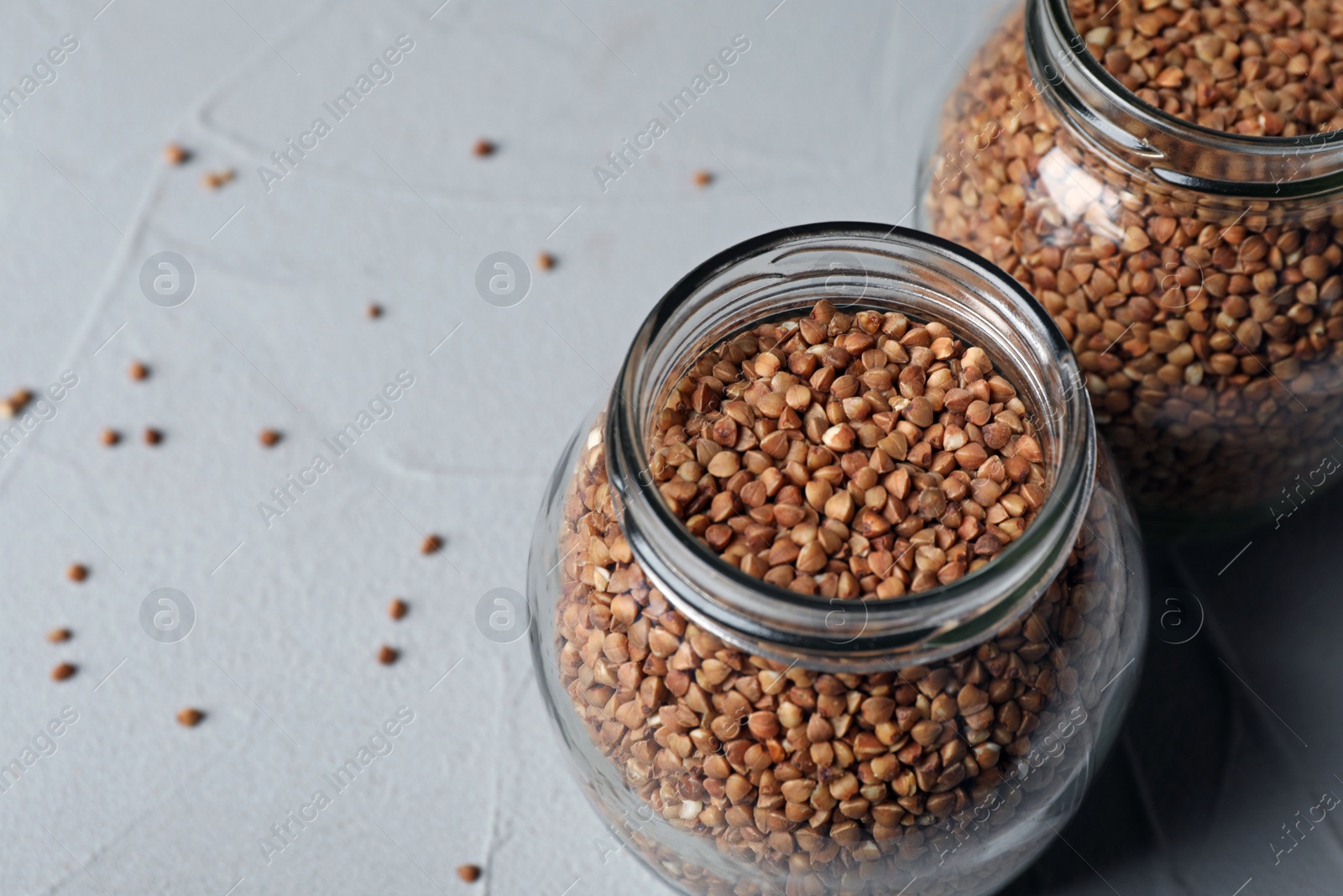 Photo of Uncooked buckwheat in glass jars on table. Space for text