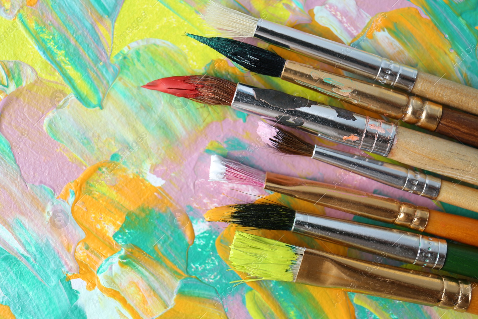 Photo of Set of different brushes on abstract colorful paint, flat lay