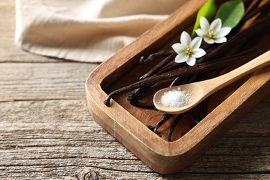 Photo of Vanilla pods, flowers, leaves and spoon with sugar on wooden table, closeup. Space for text