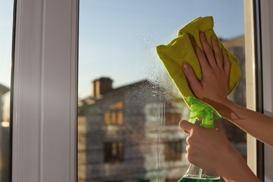 Young woman cleaning window glass with rag and detergent at home, closeup. Space for text