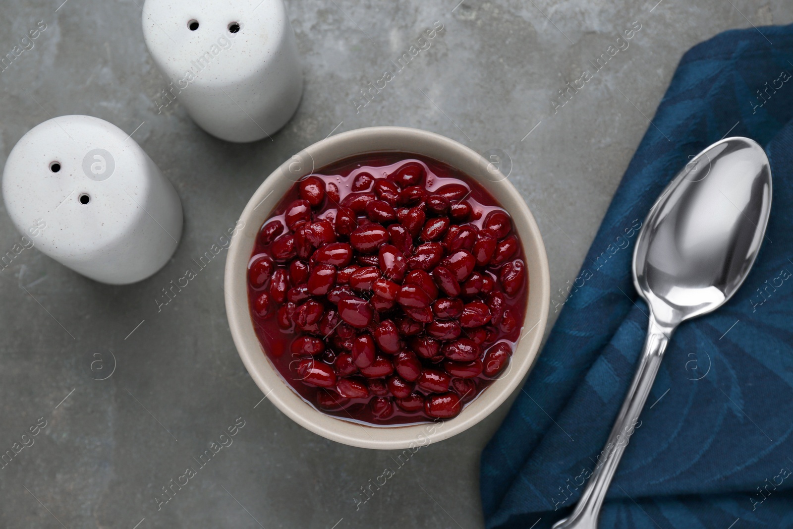 Photo of Bowl of canned kidney beans, spoon and shakers on grey table, flat lay