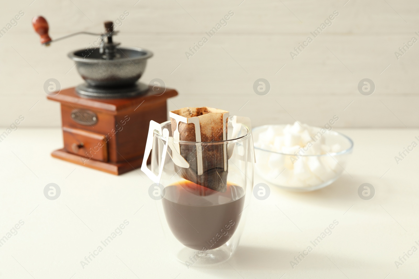 Photo of Glass with drip coffee bag on white table