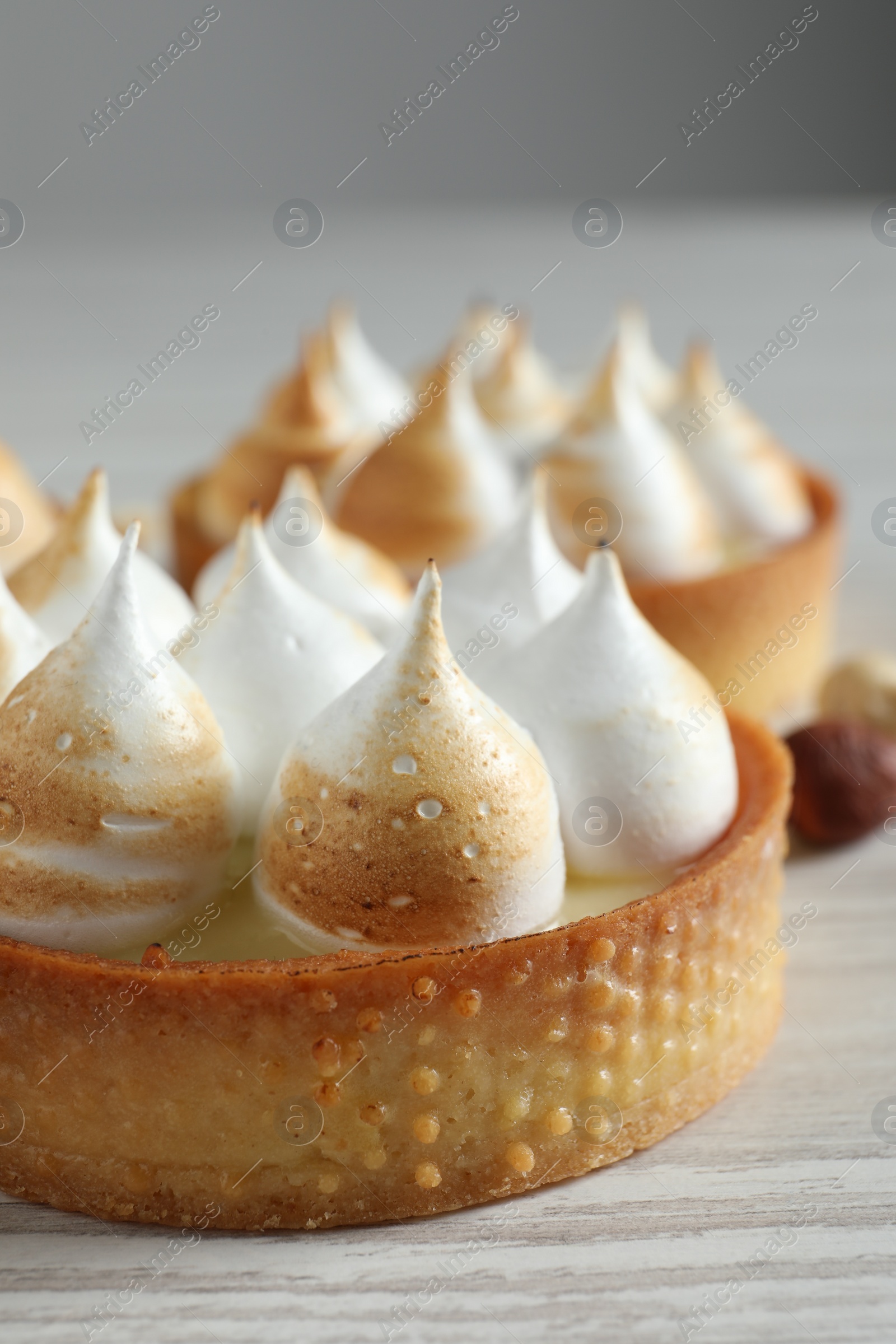 Photo of Tartlets with meringue on white wooden table, closeup. Tasty dessert