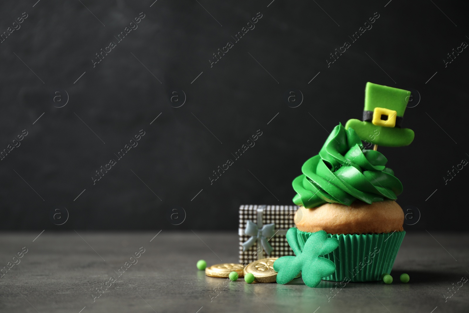 Photo of Decorated cupcake and gift box on grey table, space for text. St. Patrick's Day celebration