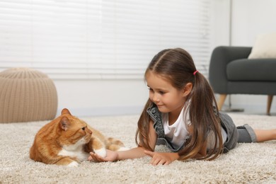 Smiling little girl and cute ginger cat on carpet at home