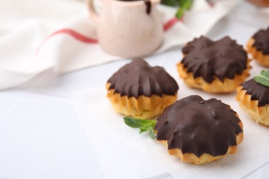 Photo of Delicious profiteroles with chocolate spread and mint on white table, closeup. Space for text
