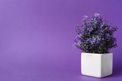 Photo of Beautiful artificial plant in flower pot on purple background, space for text