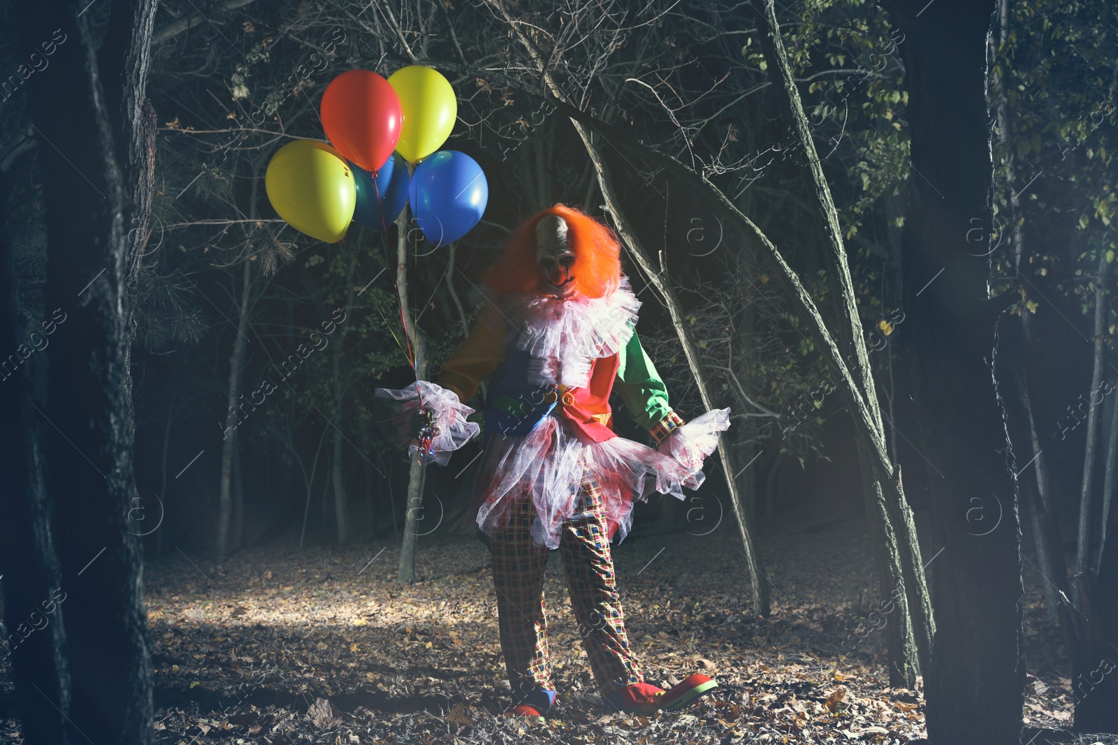 Photo of Terrifying clown with air balloons outdoors at night. Halloween party costume