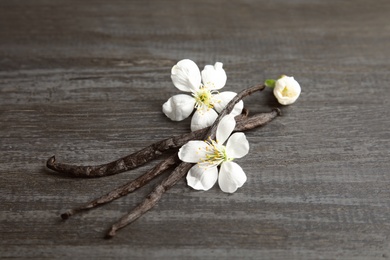 Photo of Aromatic vanilla sticks and flowers on wooden background