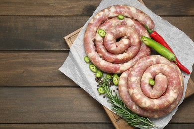 Photo of Board with homemade sausages, rosemary, chili and spices on wooden table, top view. Space for text