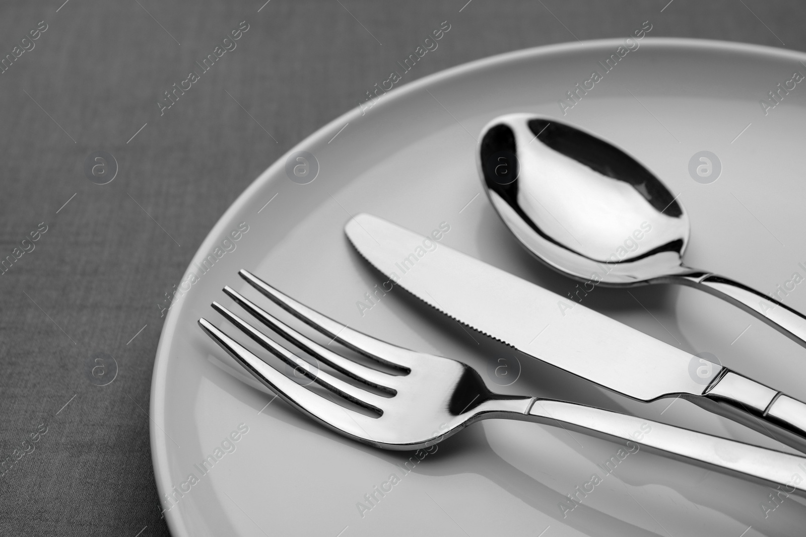 Photo of Plate with shiny silver cutlery on grey table, closeup