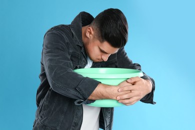 Photo of Man with basin suffering from nausea on light blue background. Food poisoning