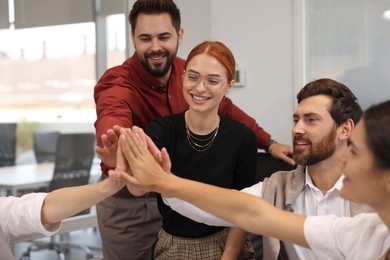 Photo of Team of employees joining hands in office