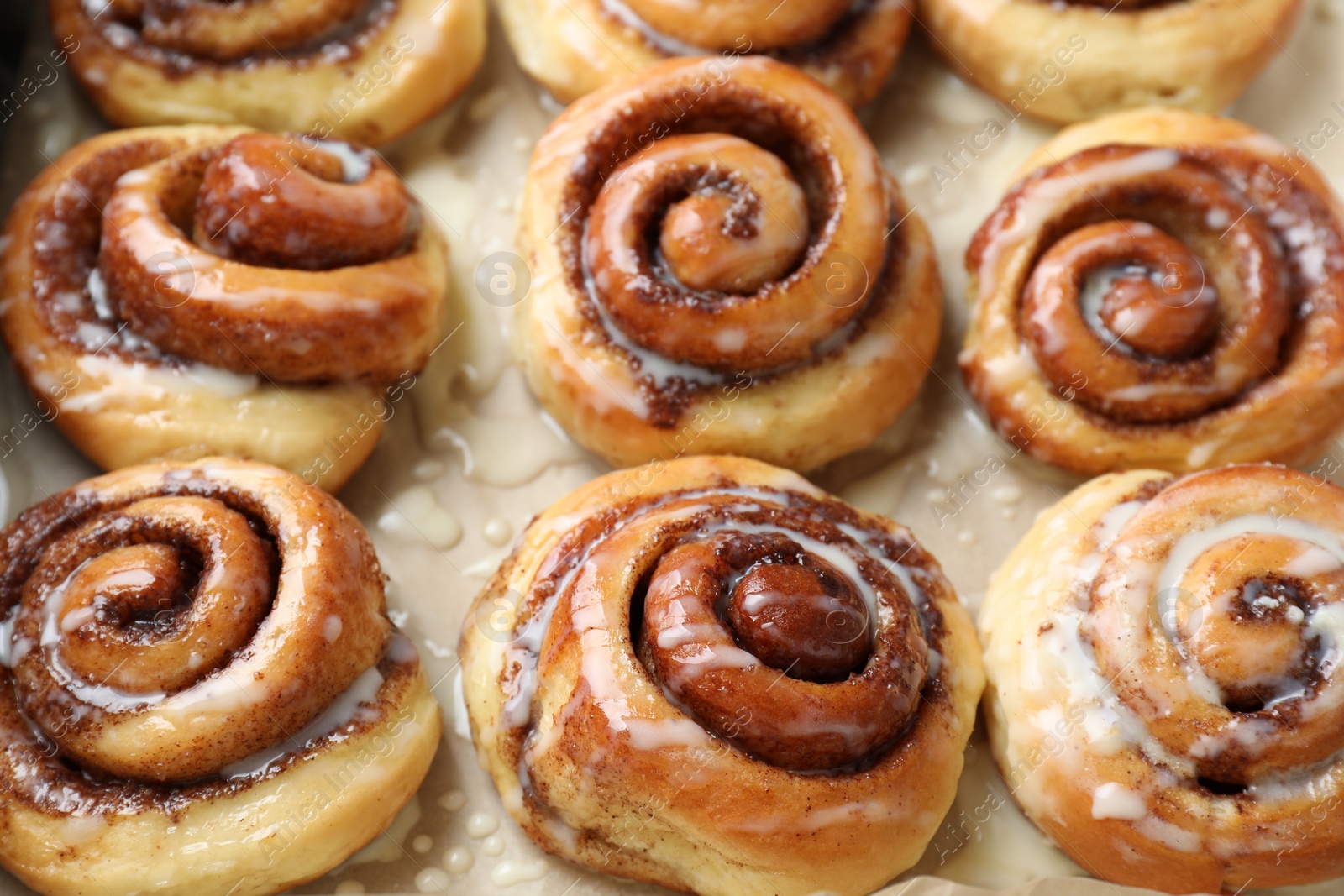 Photo of Tasty cinnamon rolls with cream on parchment paper, closeup