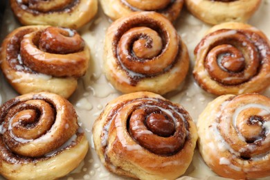 Photo of Tasty cinnamon rolls with cream on parchment paper, closeup