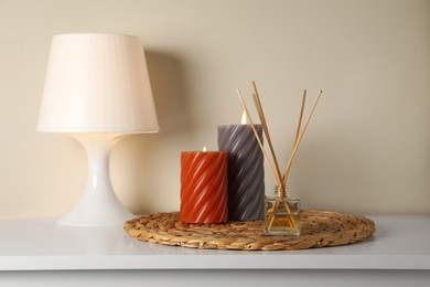 Photo of Aromatic reed air freshener, lamp and candles on white table indoors