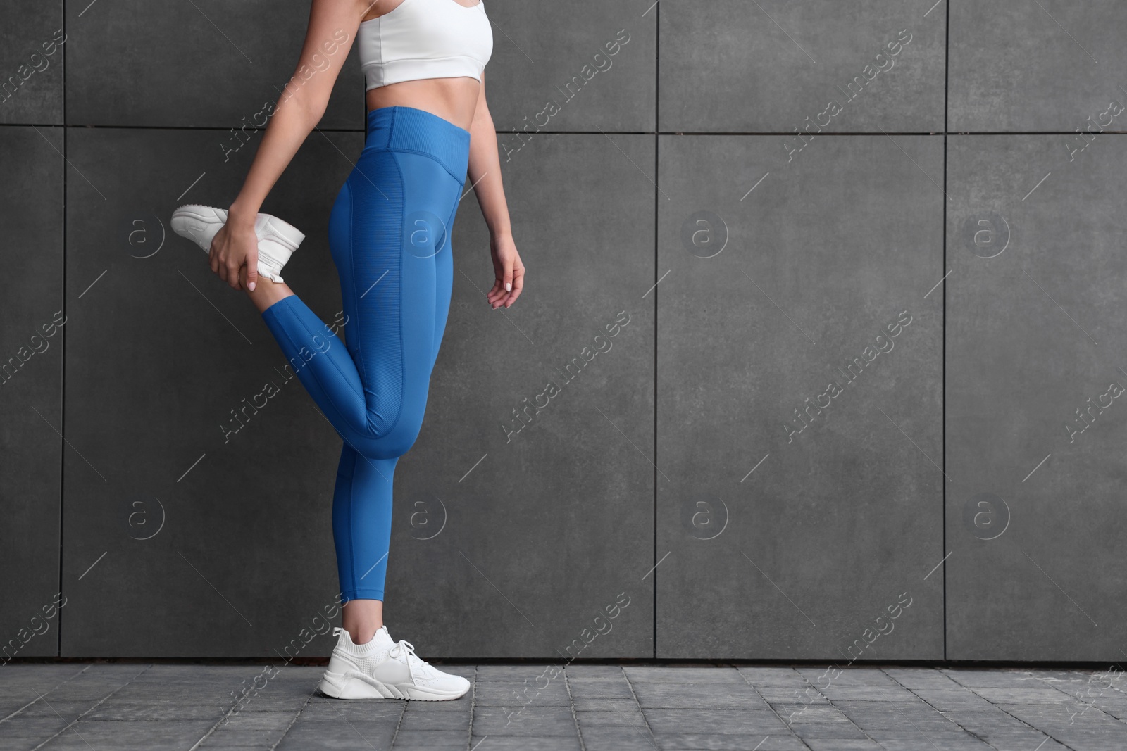 Photo of Woman in sportswear stretching near dark grey wall outdoors, closeup. Space for text