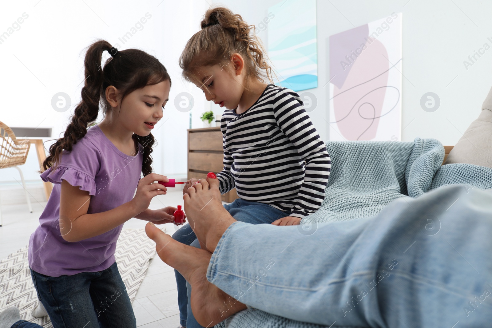 Photo of Cute little children applying polish on father's nails while he sleeping at home, closeup