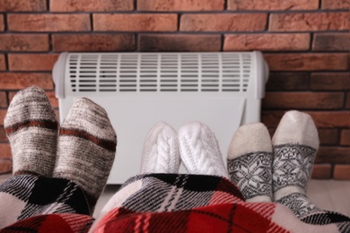 Photo of Family warming feet near electric heater at home, closeup