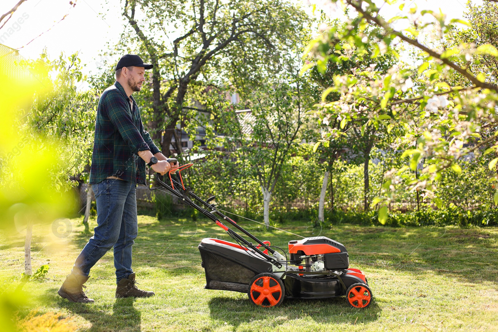 Photo of Man cutting green grass with lawn mower in garden