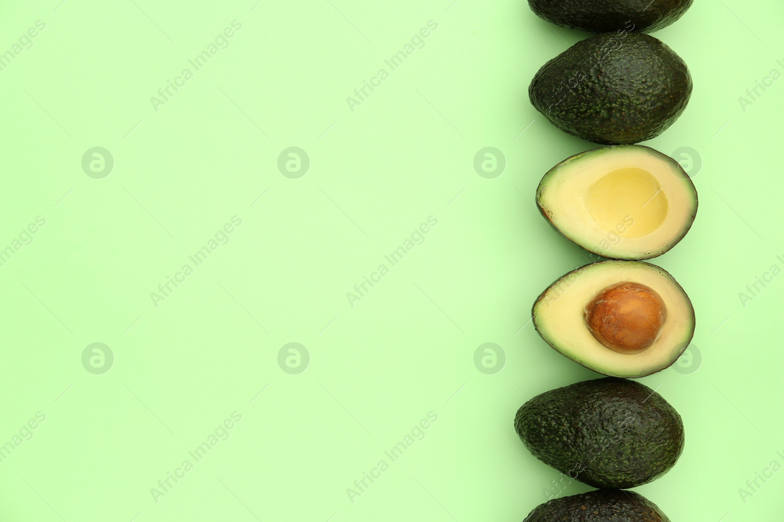 Photo of Tasty whole and cut avocados on light green background, flat lay. Space for text