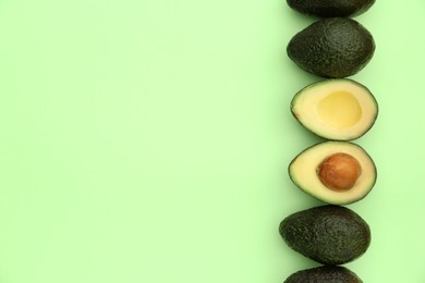 Tasty whole and cut avocados on light green background, flat lay. Space for text