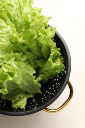 Photo of Fresh lettuce in black colander on white wooden table, top view