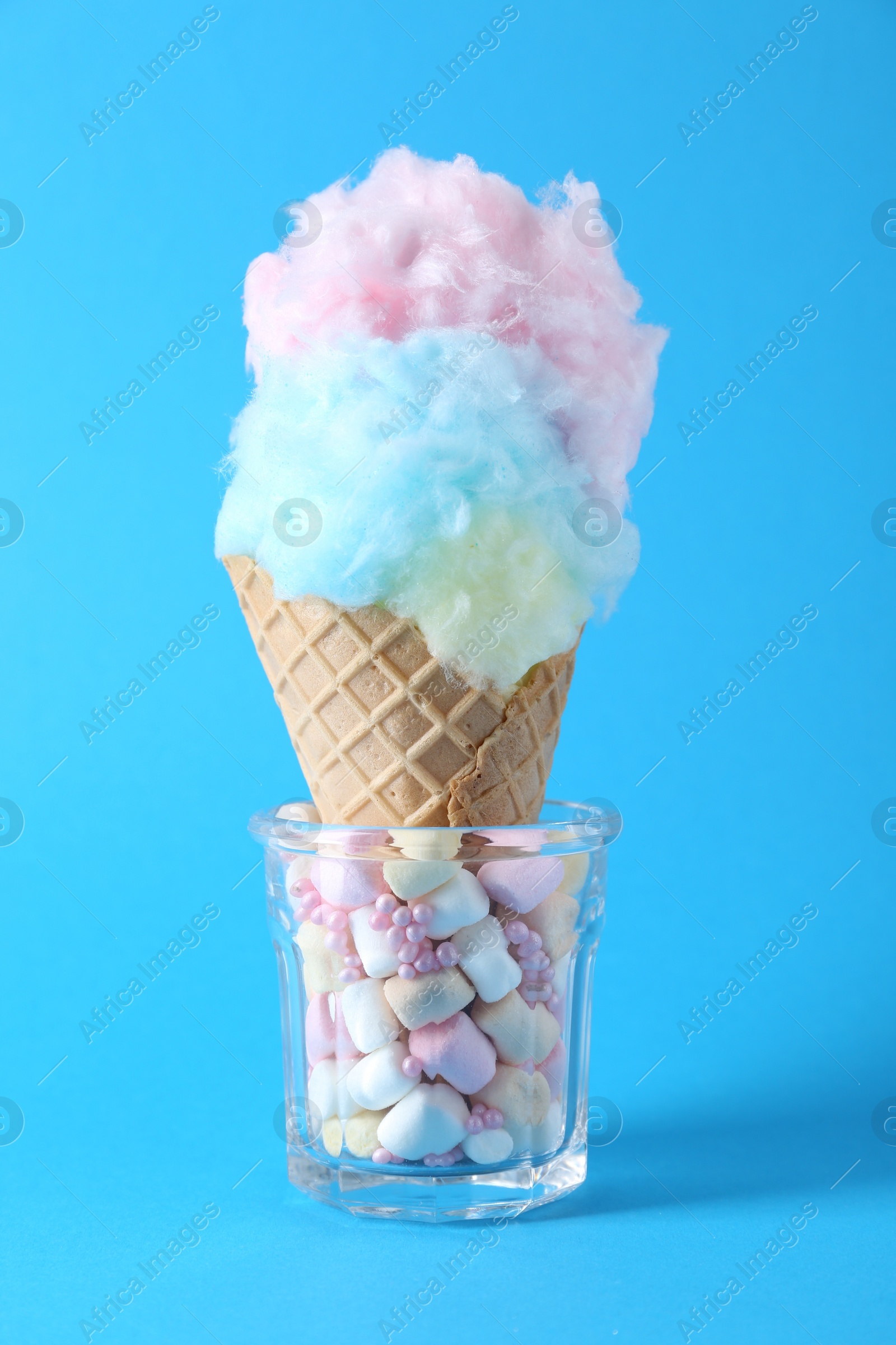 Photo of Sweet cotton candy in waffle cone on light blue background