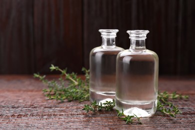 Photo of Bottles of thyme essential oil and fresh plant on wooden table, space for text