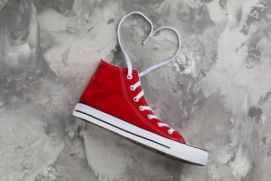 Photo of Red sneaker and white shoe lace in shape of heart on grey stone table, top view