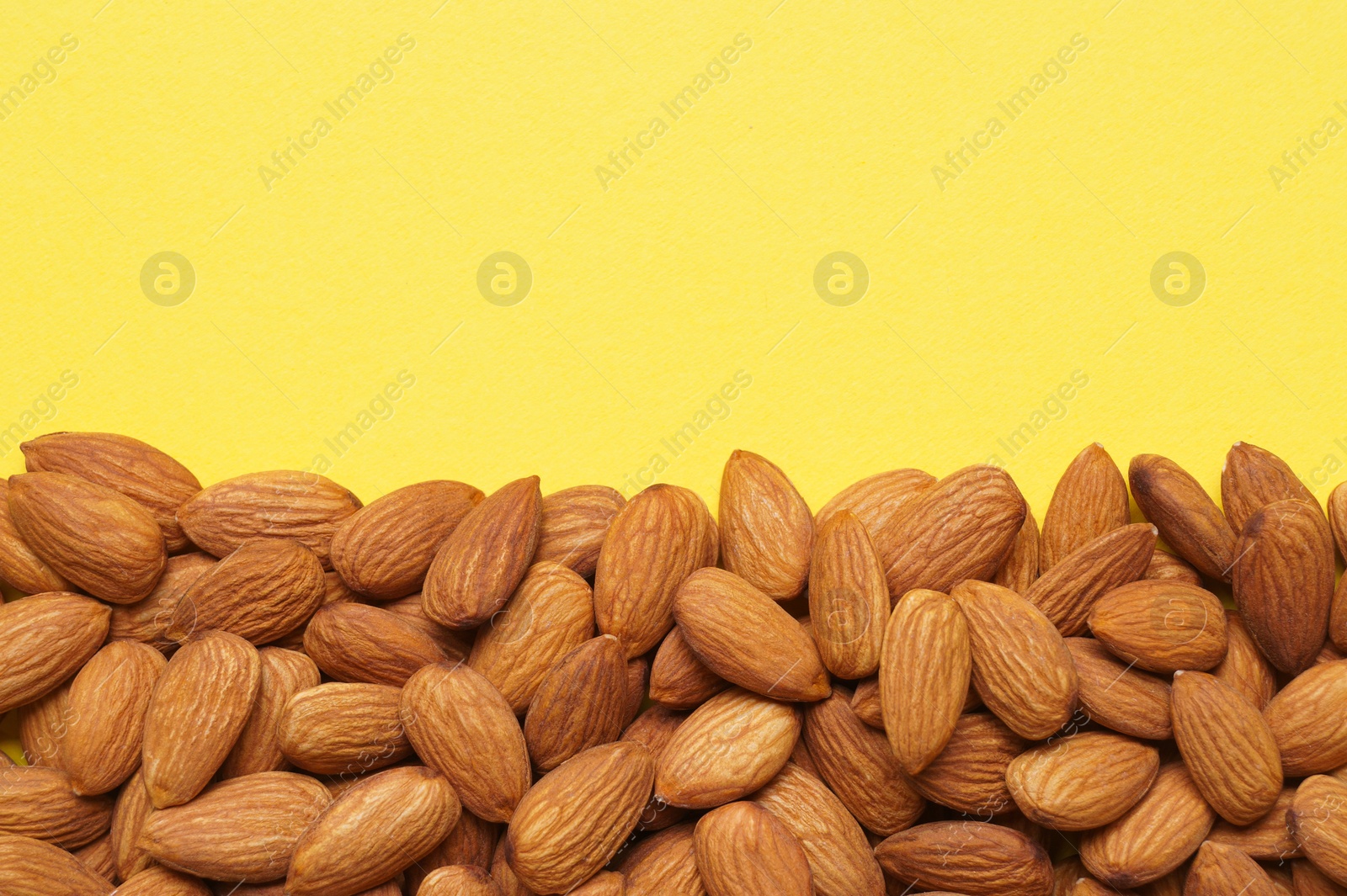 Photo of Delicious raw almonds on yellow background, flat lay. Space for text