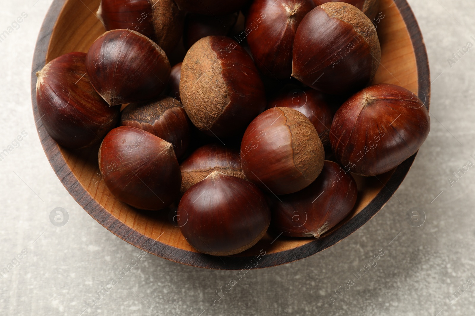 Photo of Roasted edible sweet chestnuts in bowl on light grey table, top view