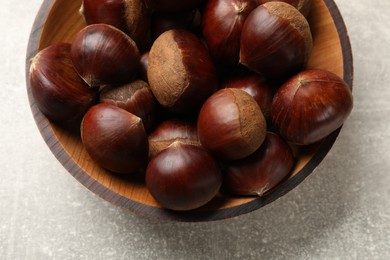 Roasted edible sweet chestnuts in bowl on light grey table, top view