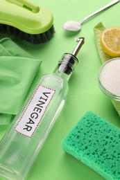 Photo of Eco friendly natural cleaners. Vinegar in bottle, soda, sponge, brush and gloves on green background