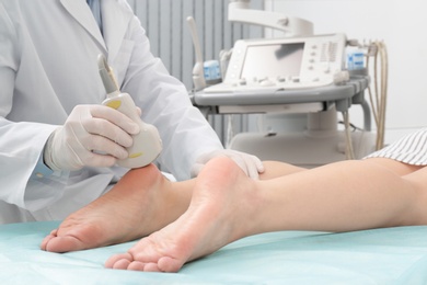 Photo of Doctor conducting ultrasound examination of patient's foot in clinic, closeup