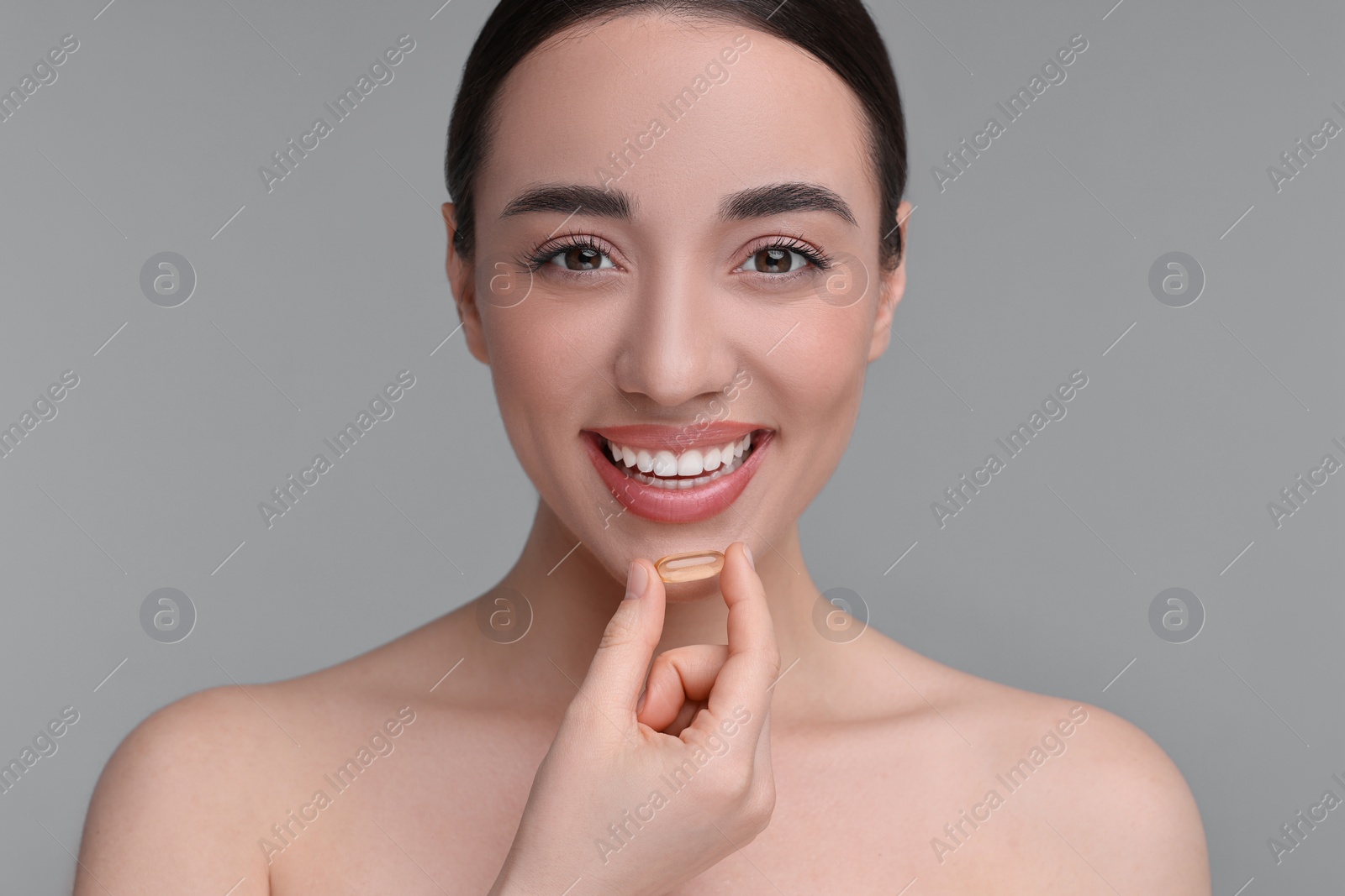 Photo of Beautiful young woman with vitamin pill on grey background