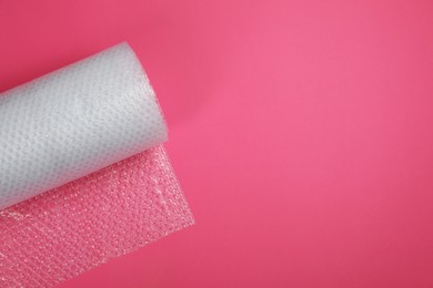 Photo of Bubble wrap roll on pink background, top view. Space for text