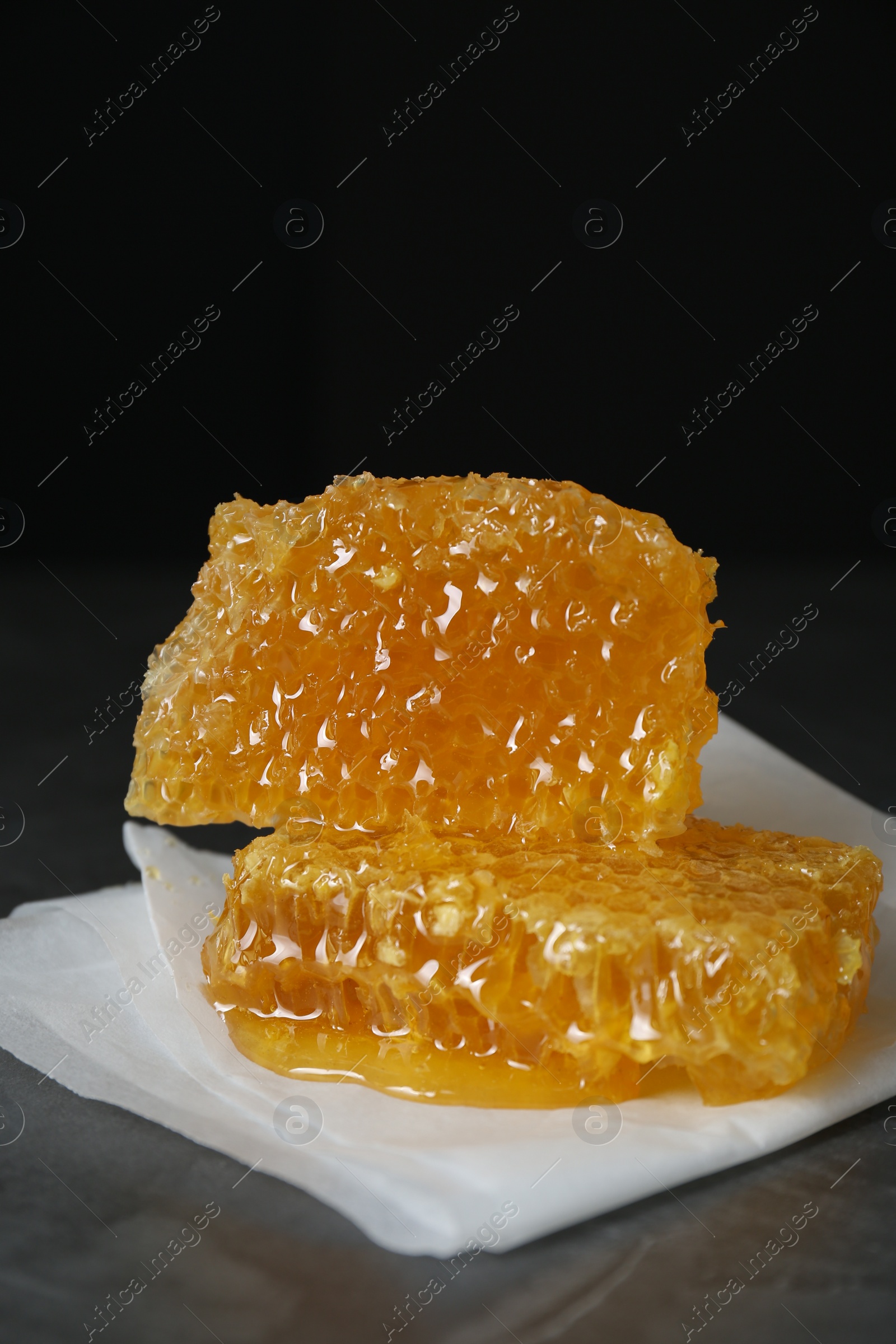 Photo of Natural honeycombs on dark table against black background, space for text