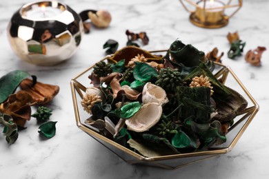 Aromatic potpourri of dried flowers in bowl on white marble table, closeup