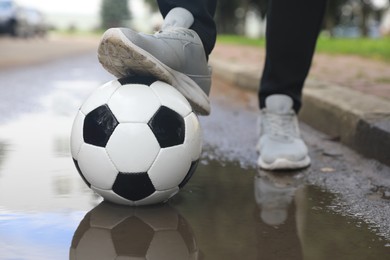 Man with soccer ball near puddle outdoors, closeup