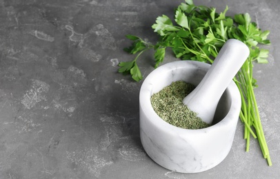 Photo of Mortar with dry parsley and space for text on grey table