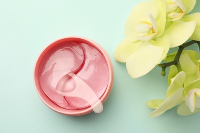 Jar of under eye patches with spoon and flowers on turquoise background, flat lay. Cosmetic product