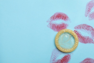 Photo of Condom with lipstick kiss marks and space for text on light blue background, top view. Safe sex