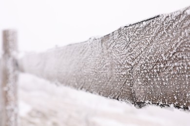 Wooden fence covered with hoarfrost outdoors on snowy day, closeup