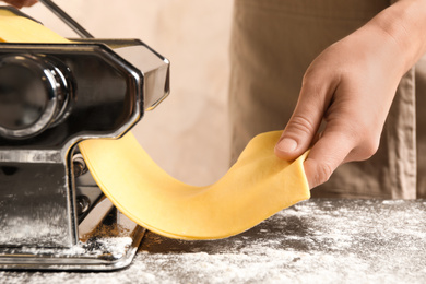 Photo of Woman preparing dough with pasta maker machine at table, closeup