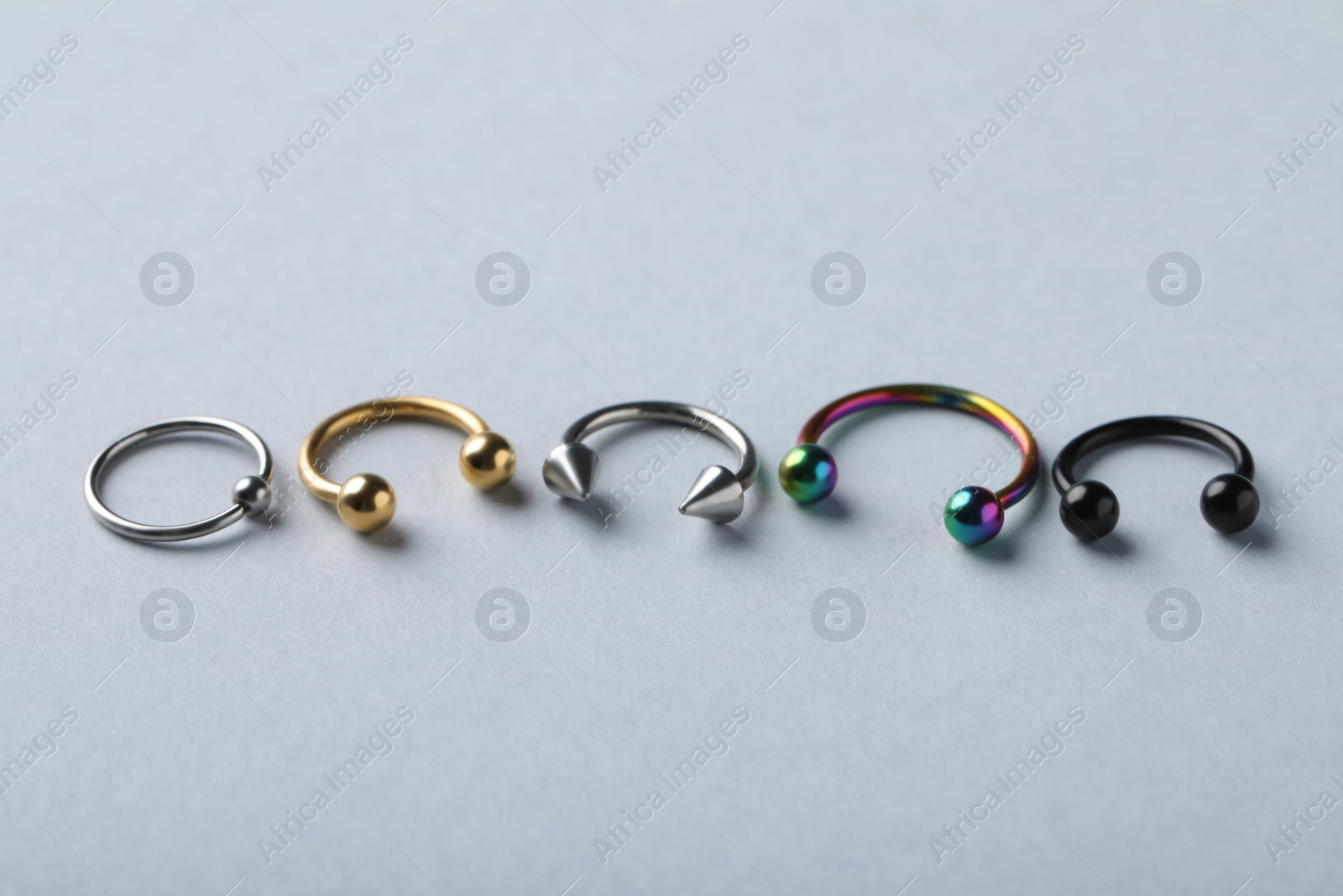 Photo of Stylish captive bead and horseshoe rings on light grey background. Piercing jewelry