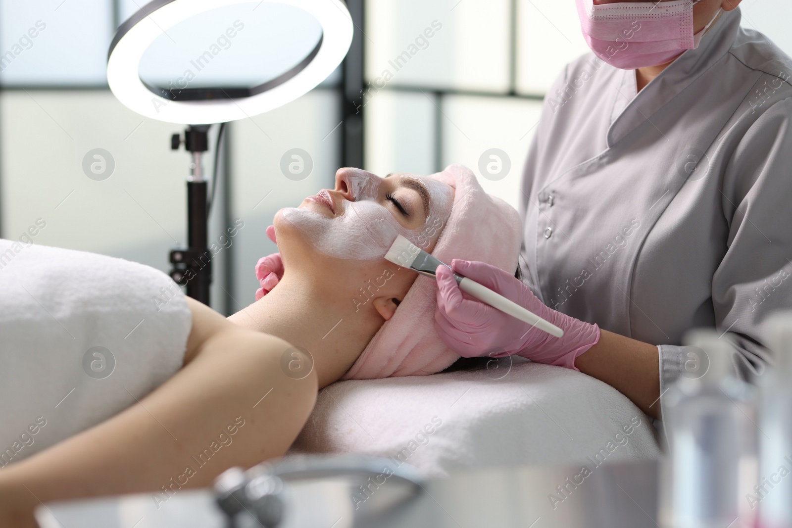 Photo of Cosmetologist applying mask on woman's face in clinic, closeup